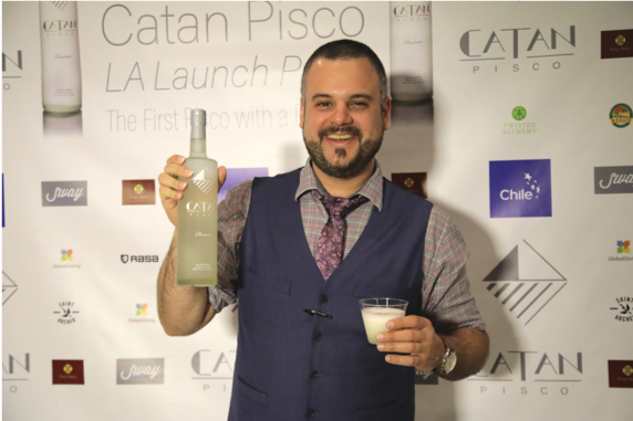 Person smiling and standing with cocktail and bottle of Catan Pisco.