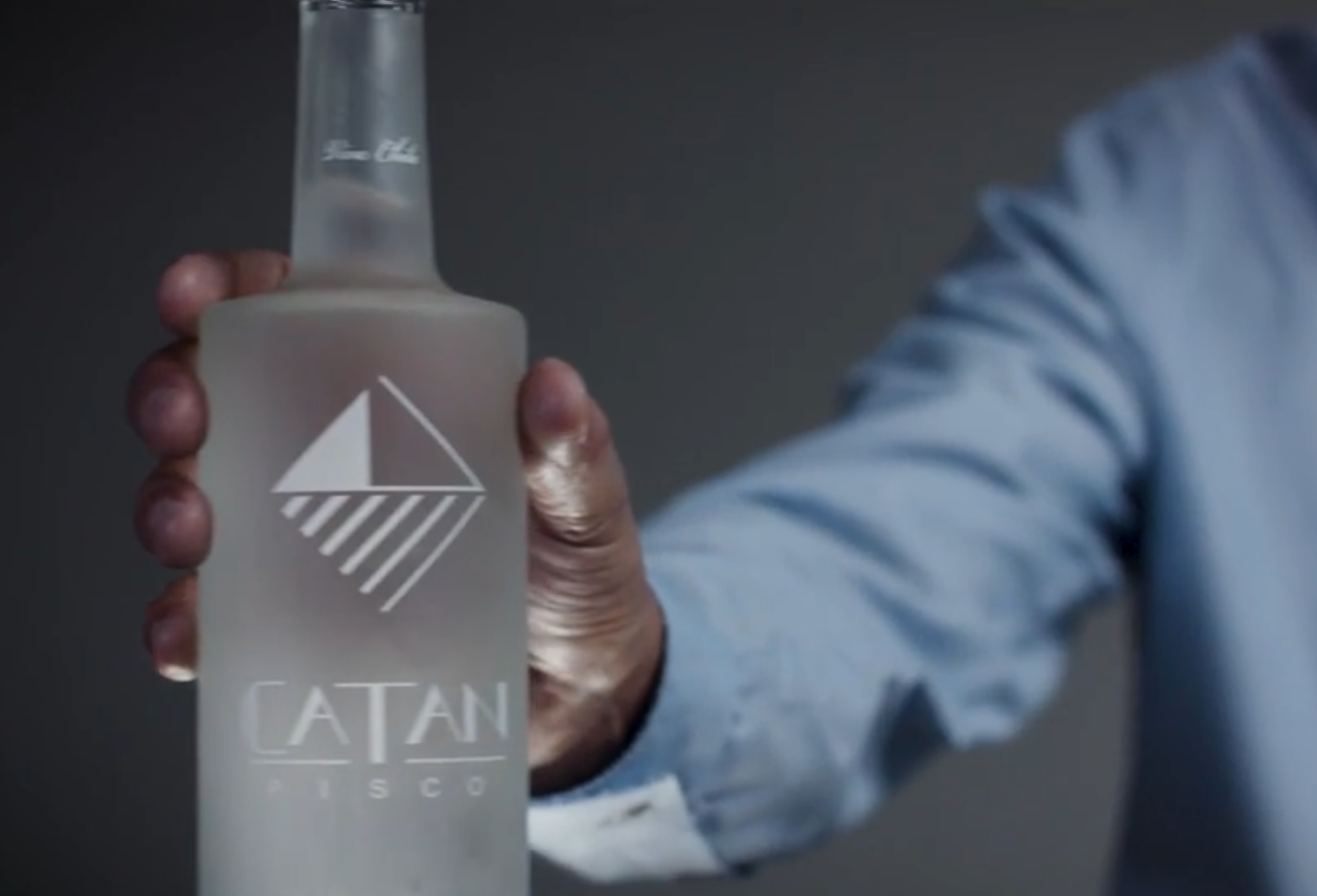 A person in a blue shirt holding a bottle of Catan Pisco.